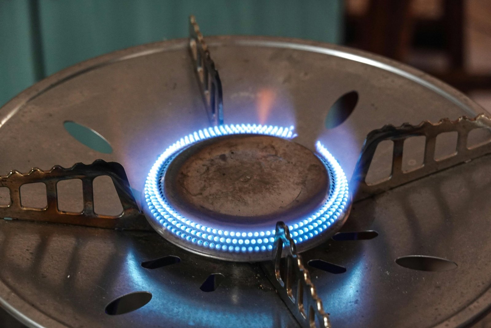 A detailed view of a lit gas stove burner with visible blue flames and metal support.